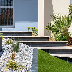 Aménagement paysager moderne avec escaliers, galets, gazon artificiel et plantes luxuriantes près d'une maison à Allainville près d'Ablis dans les Yvelines 78