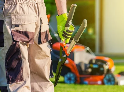 Jardinier avec des ciseaux de taille et une tondeuse à gazon orange en arrière-plan à Allainville près d'Ablis dans les Yvelines 78