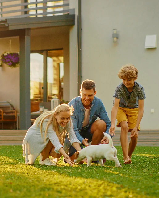 Famille souriante jouant avec un chiot blanc dans le jardin.